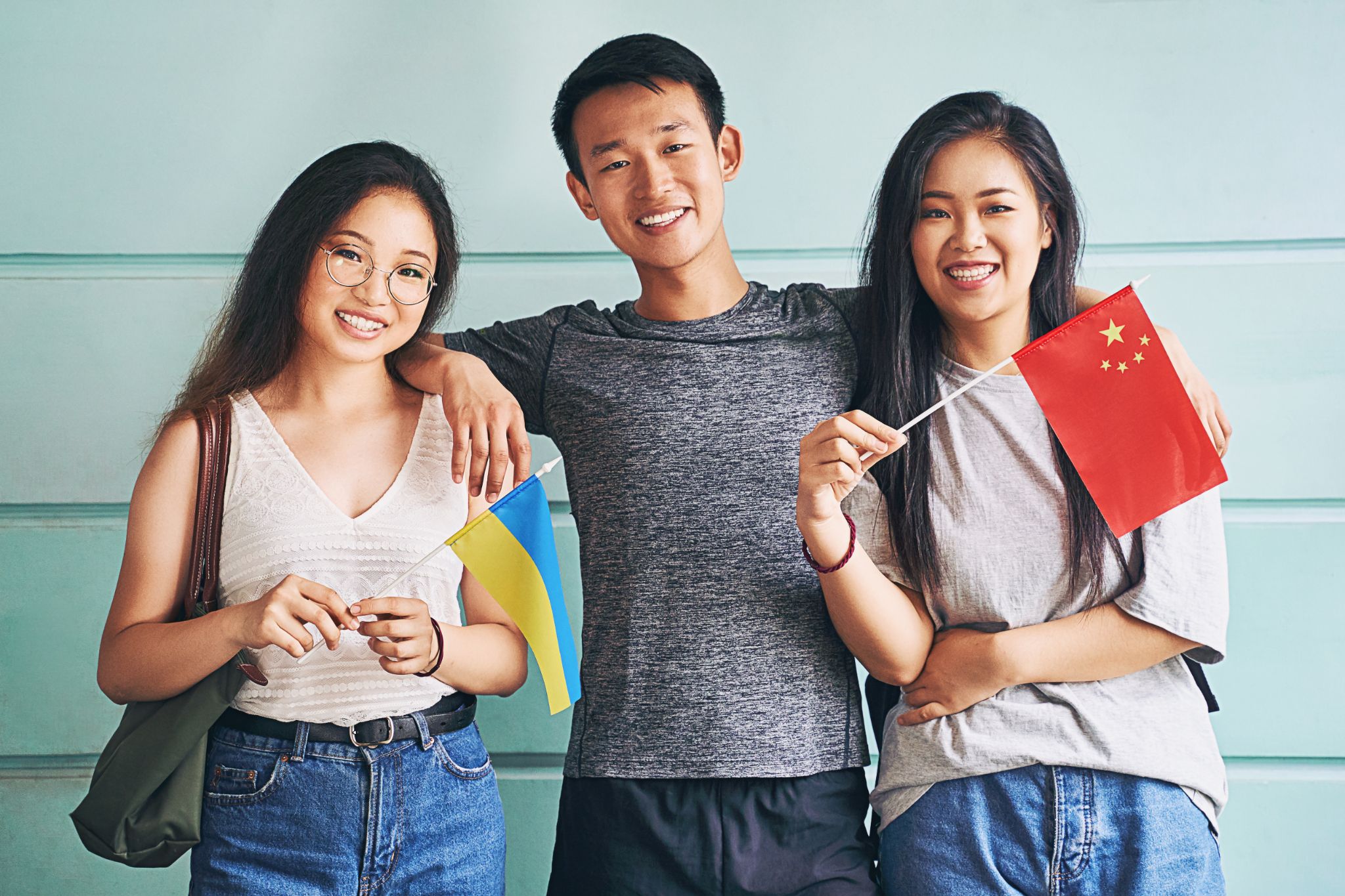 Group of three asian students smiling and holding flags of China and Ukraine