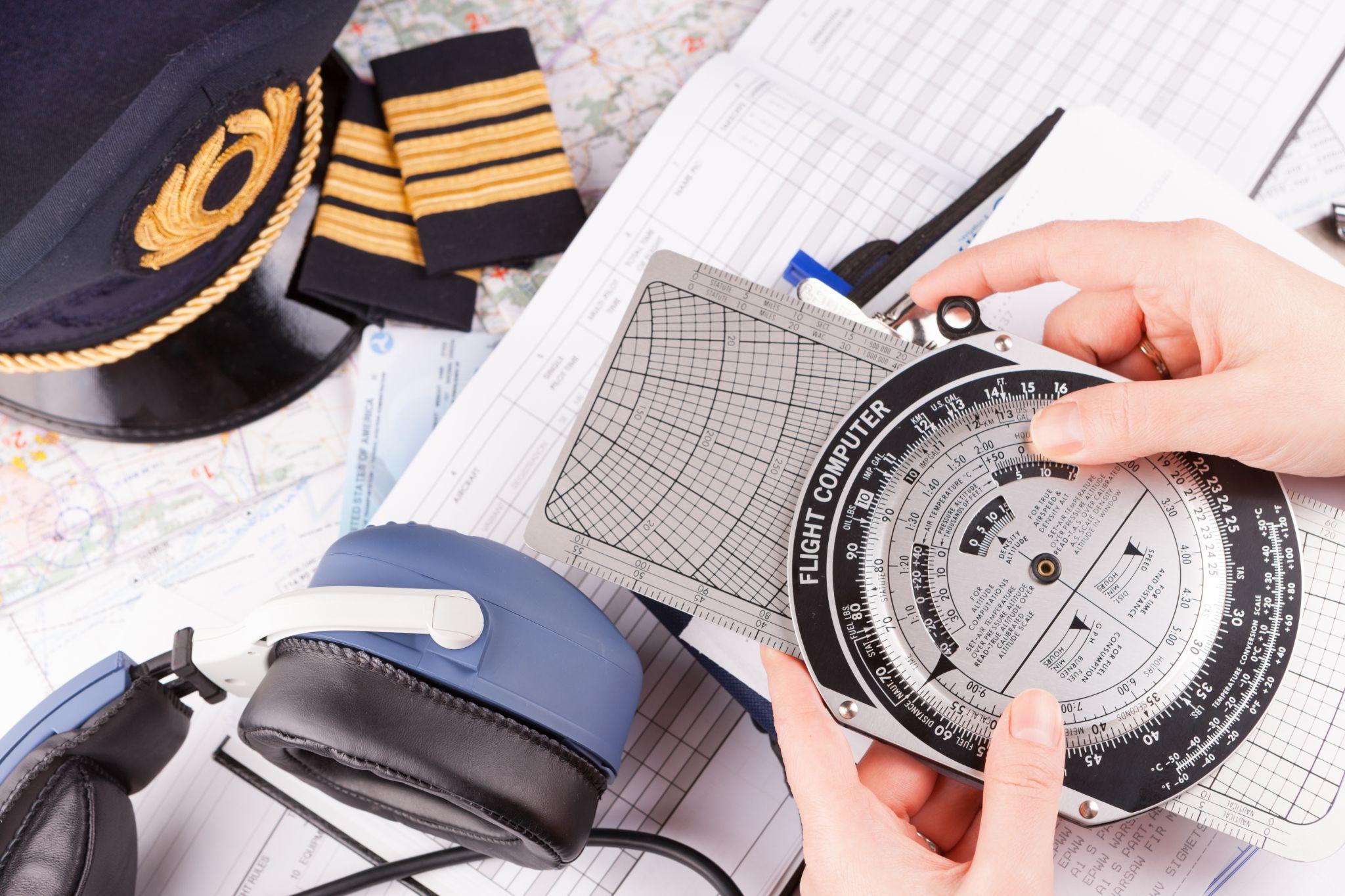 pilot hand holding flight computer and making pre-flight calculations with equipment including hat