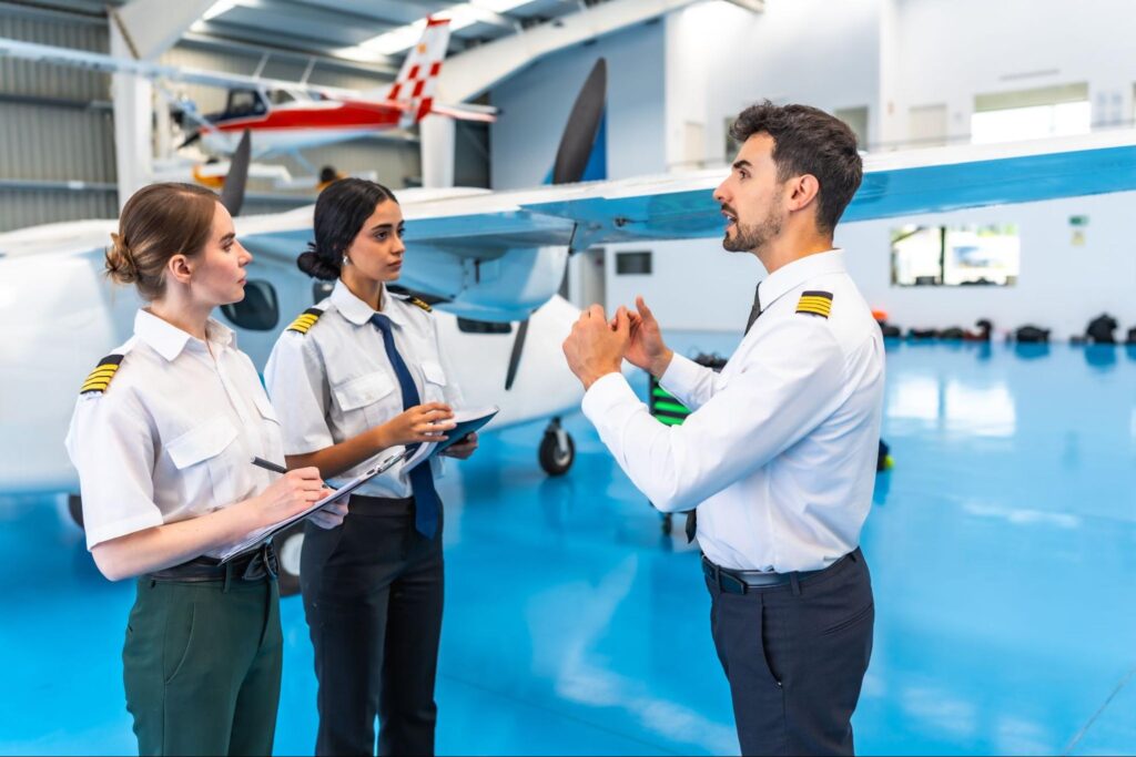 Flight instructor training pilots in hangar setting.