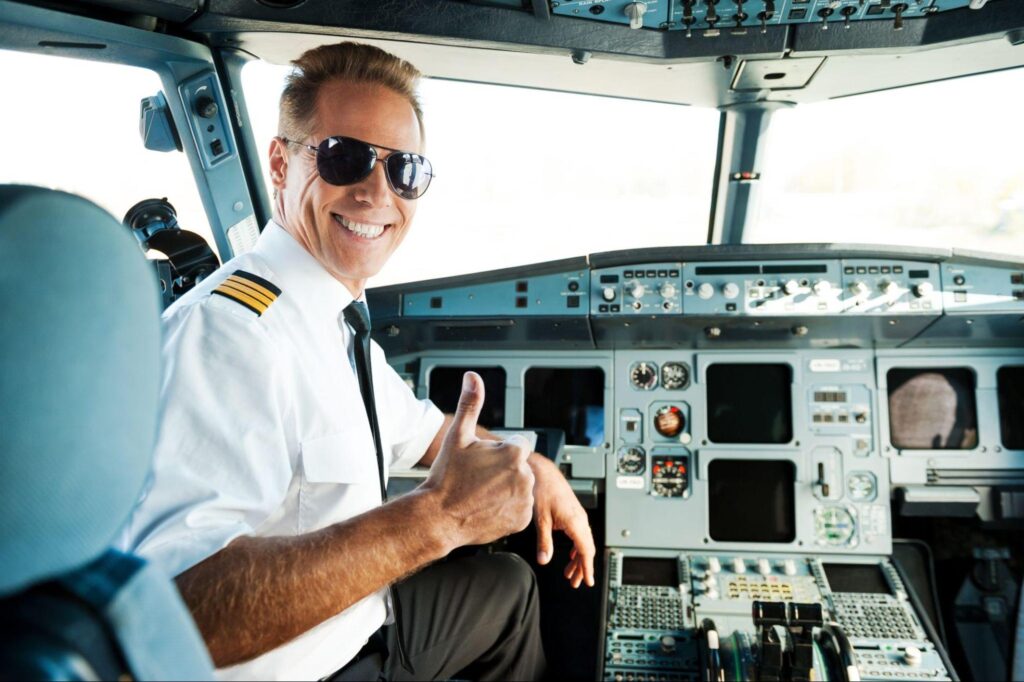 Rear view of confident male pilot showing his thumb up and smiling while sitting in cockpit.