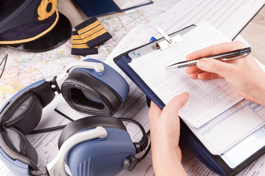 Airplane pilot hand filling in an pre-fligh checklist with equipment including hat, epaulettes and other documents