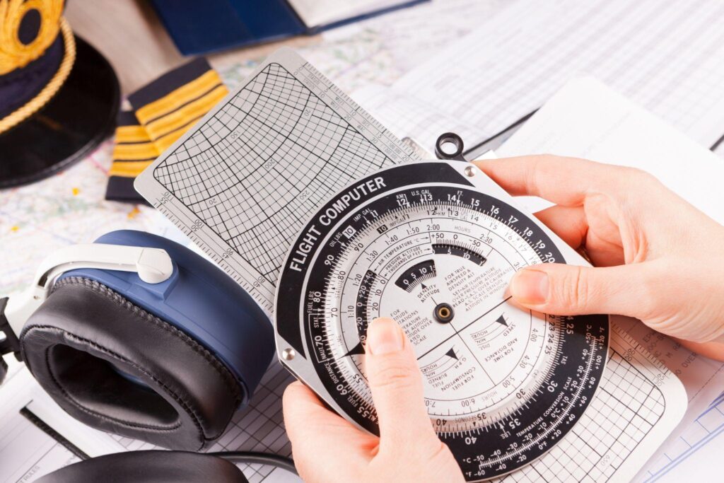 an airplane pilot hand holding flight computer and making pre-flight calculations with equipment including hat, epaulettes and other documents in background