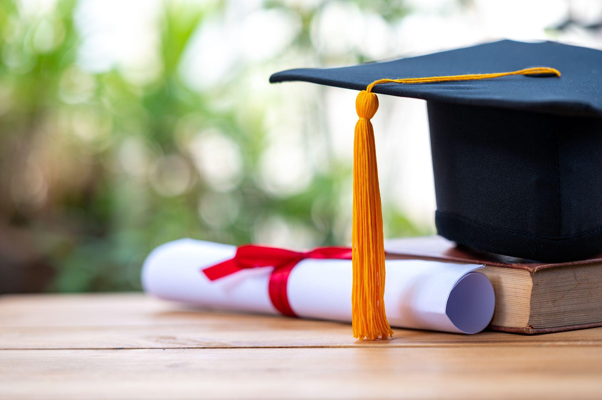 A black graduation cap and a certificate placed on an old book