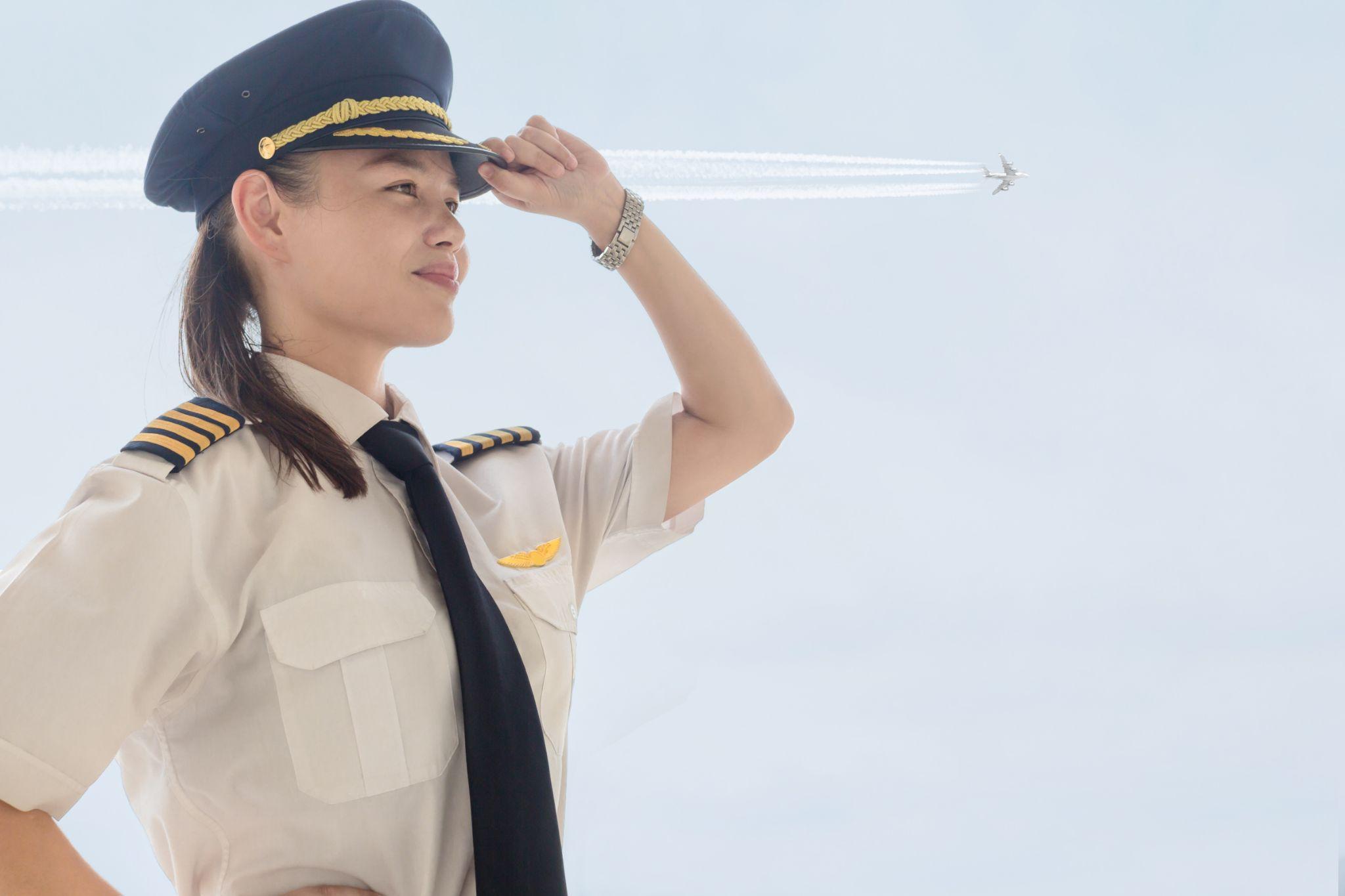 A pretty female pilot standing next to a airplane at the airport.