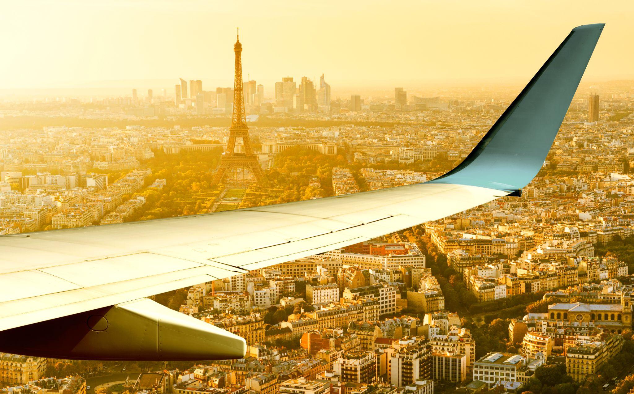 Airplane flying over Paris, view of Eiffel tower from plane window at sunset.