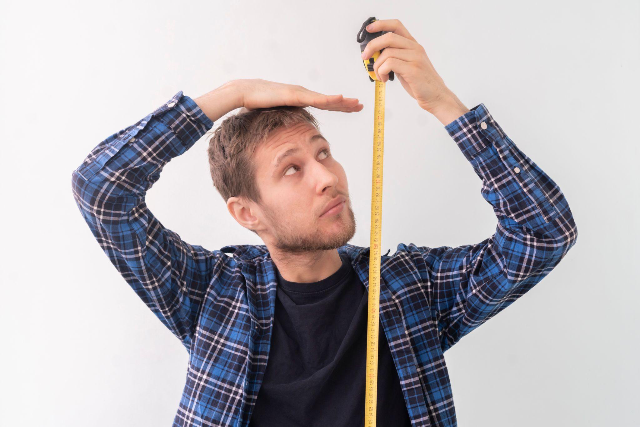 male person with a roll tape measure the height against the wall