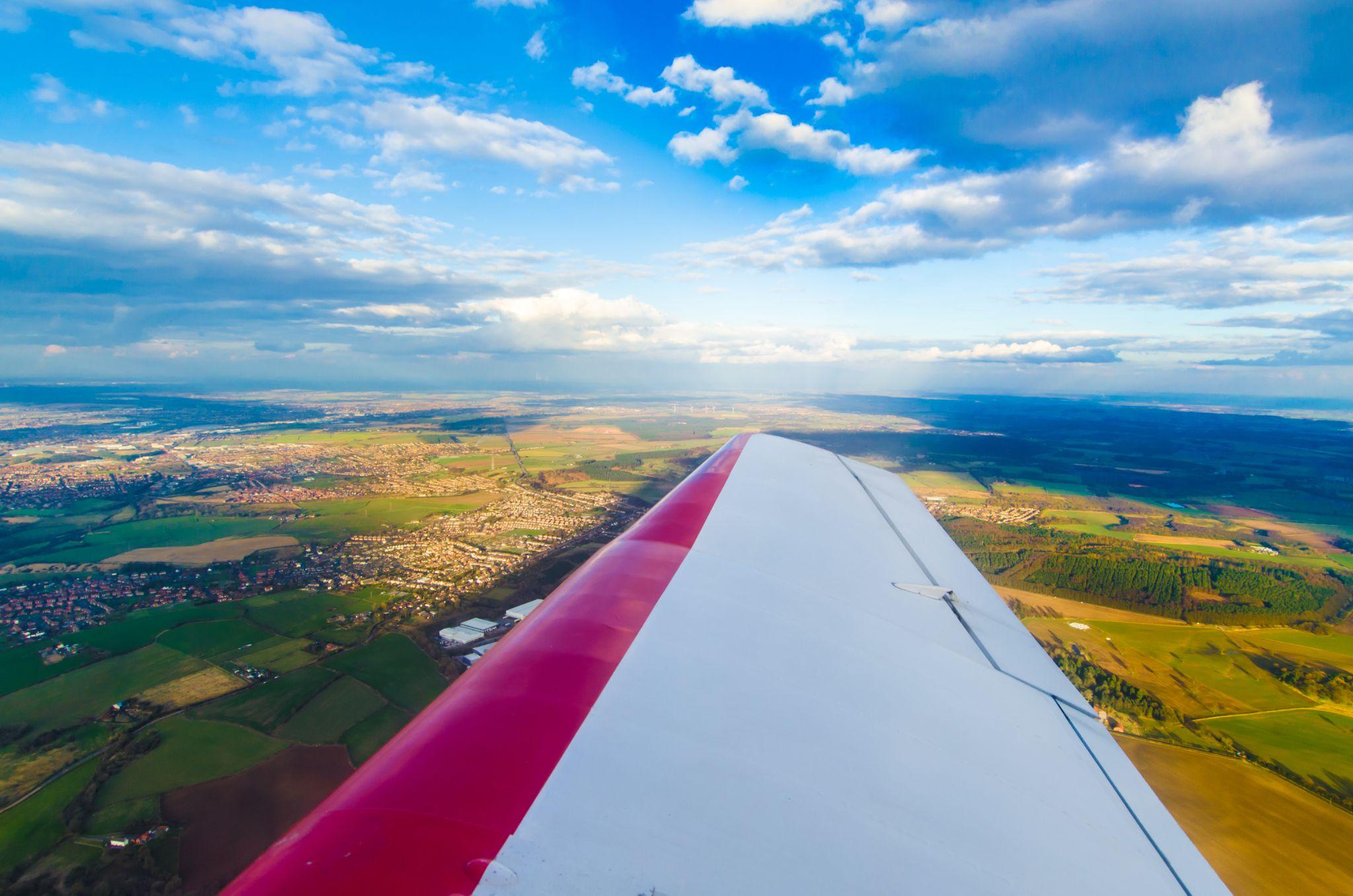 Aerial view of a plane wing flying over green fields