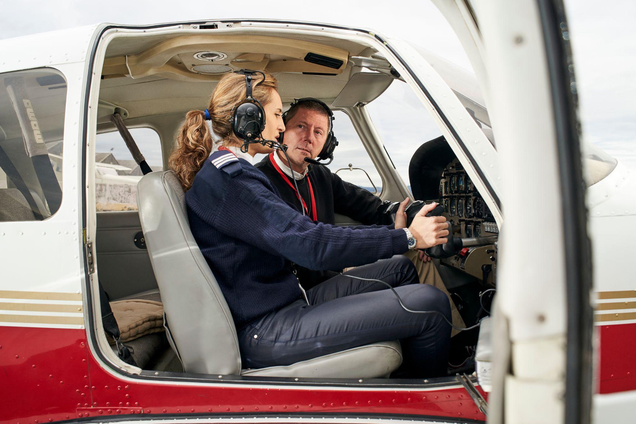 Pilot in training and flight instructor in the cockpit of an airplane. Female pilot with headphones preparing to fly.