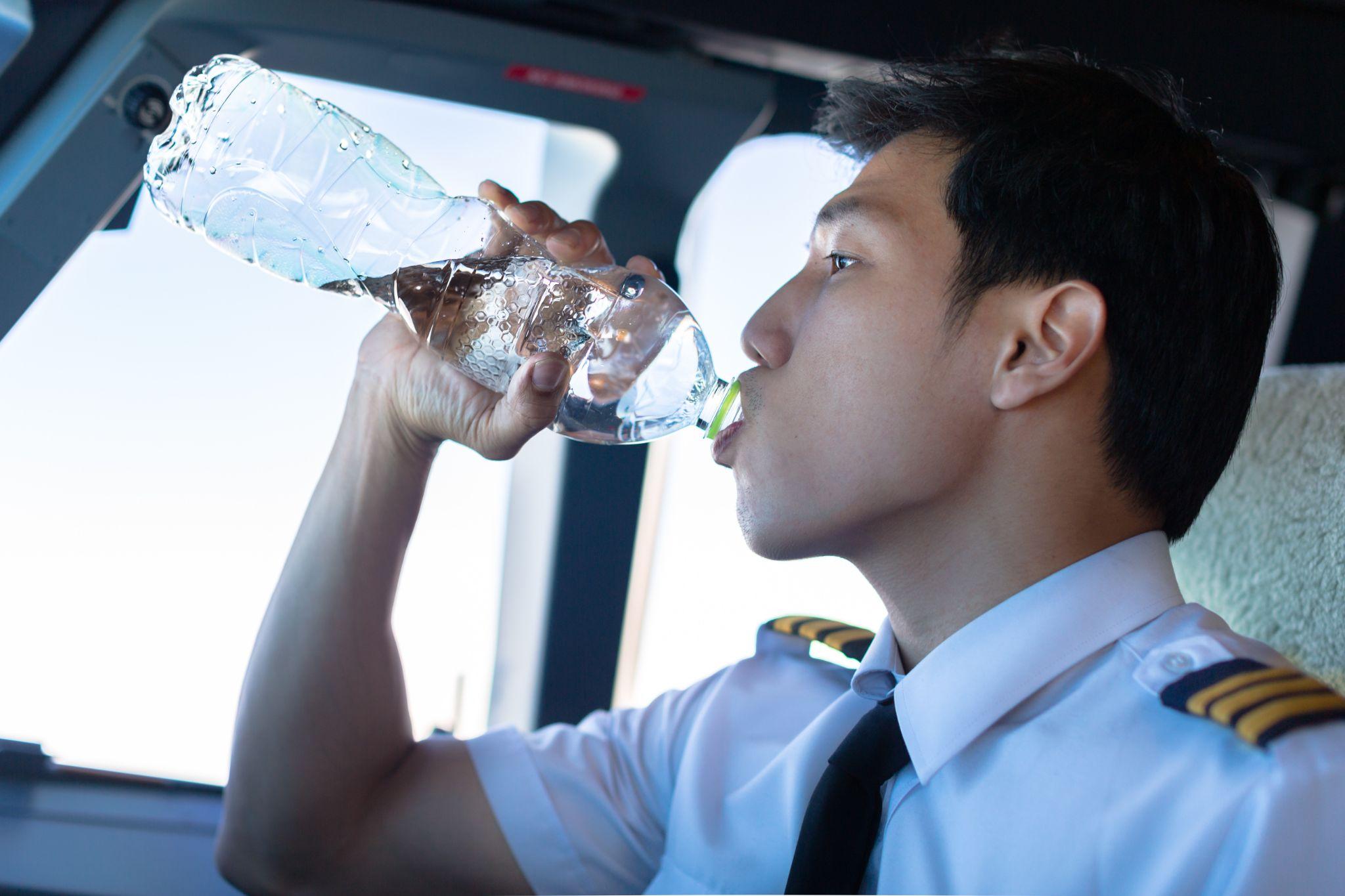 Pilot man drinking water in the airplane.