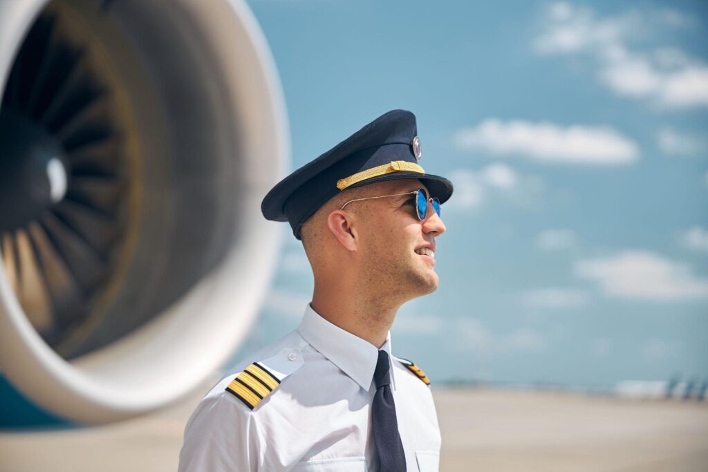 Pilot smiling in sunglasses standing outdoors in airfield next to airplane jet