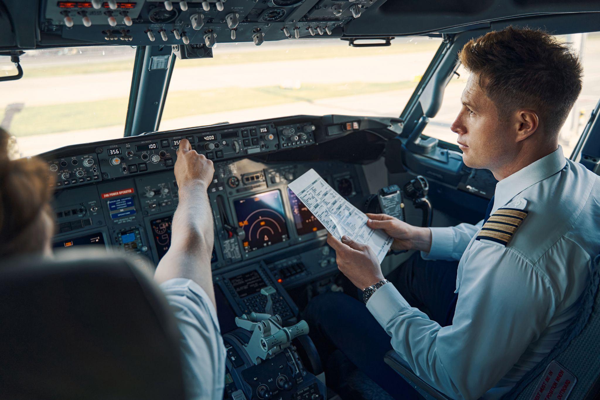 Airline captain and first officer sitting in the cockpit with flight checklist.