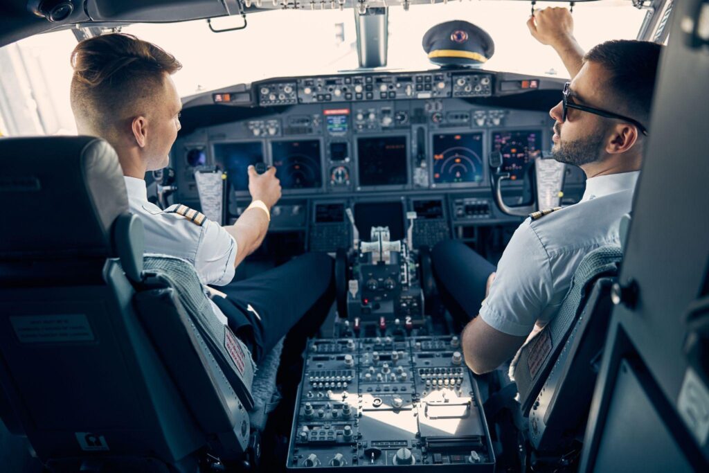 Two handsome pilots sitting on the chairs in a cockpit.