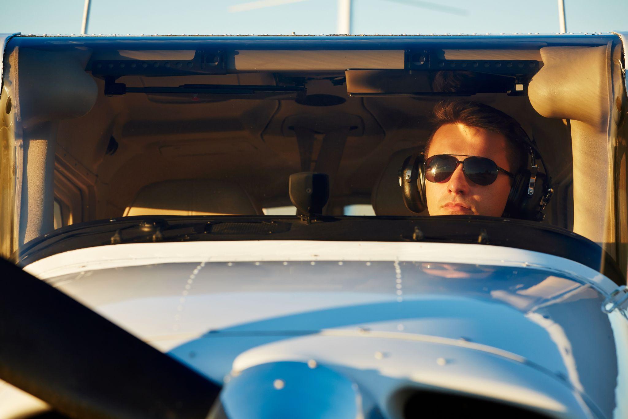 International student pilot in a cockpit wearing a headset and sunglasses during flight training.