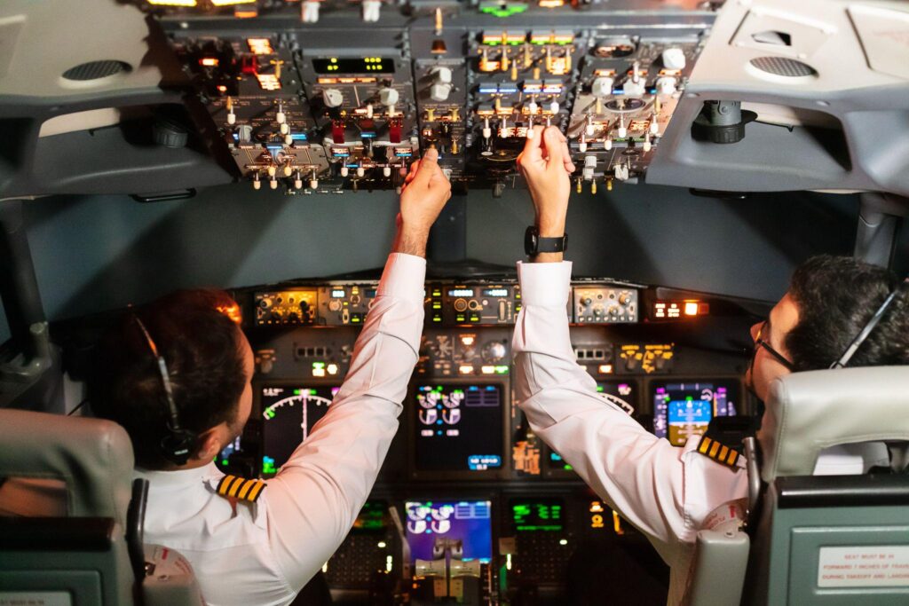 Two international pilots operate flight controls inside a commercial cockpit.